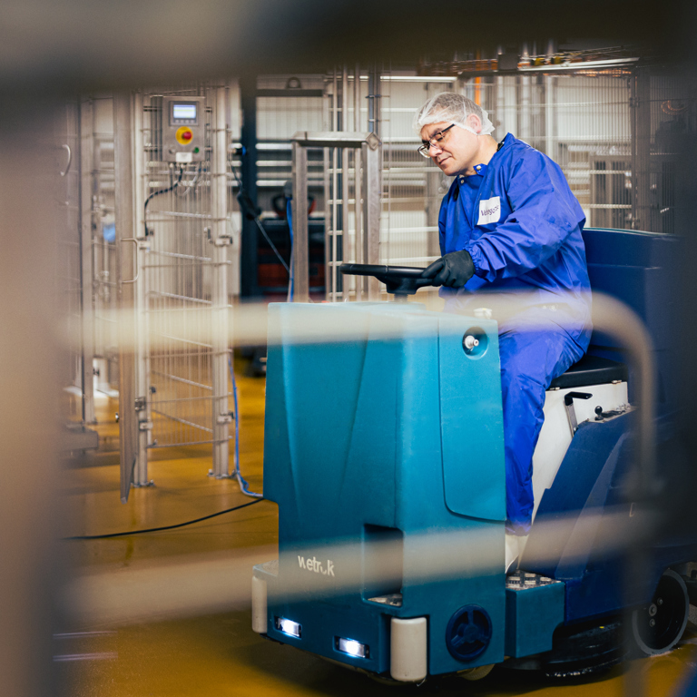 Een persoon reinigt de vloer van een faciliteit in de voedingsindustrie met behulp van een schoonmaakwagen